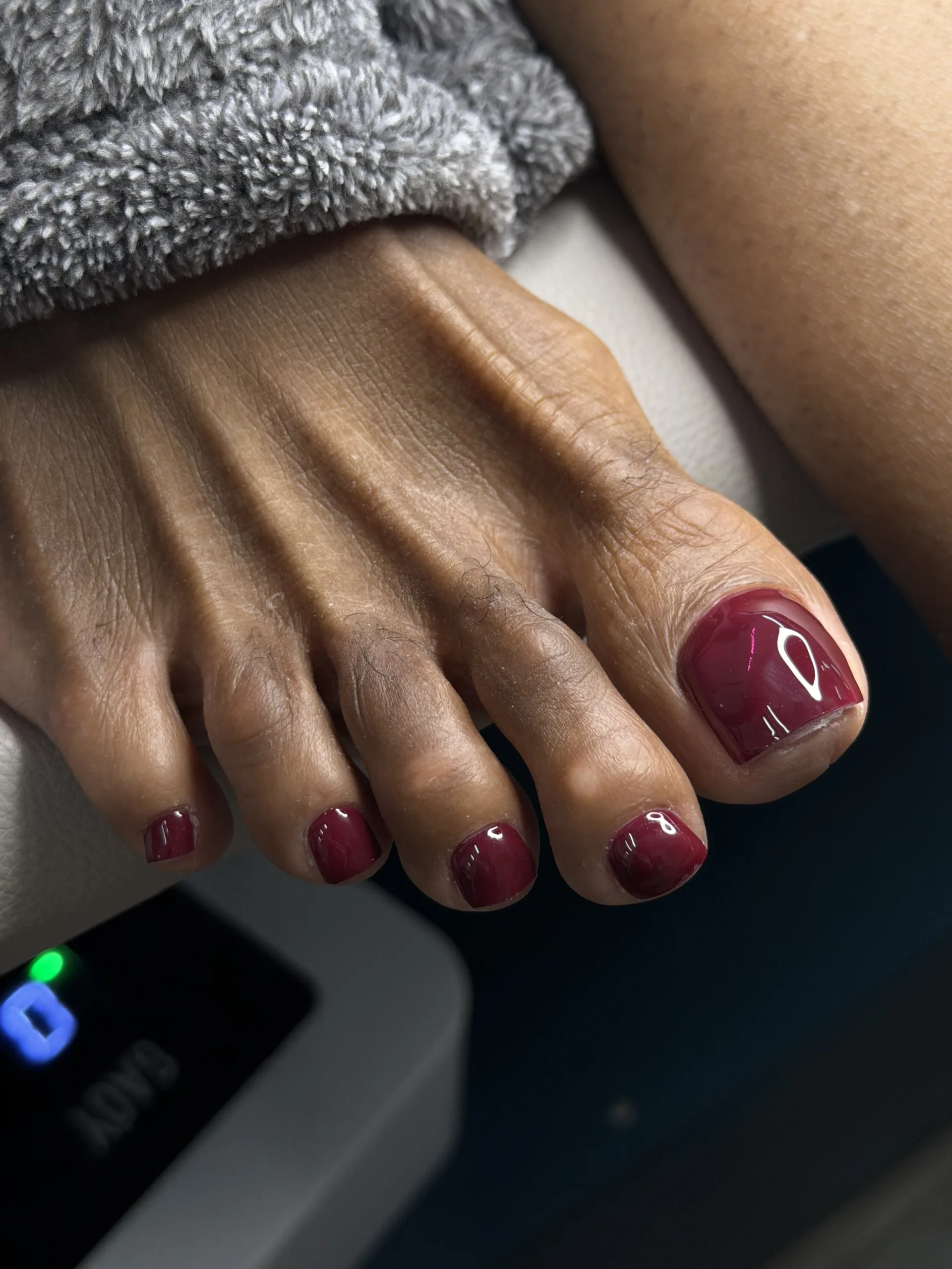 Deep burgundy gel pedicure with a glossy finish on short, carefully shaped toenails